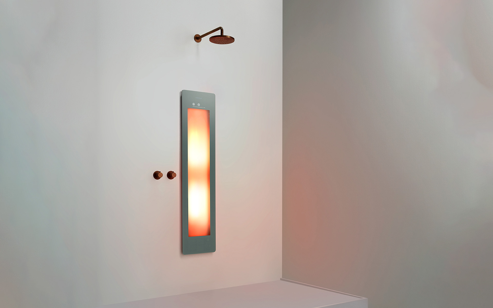 A sage-green Sunshower panel glowing warm orange in infrared mode, on the plain white wall of a shower recess with a bronze rain head above and two bronze controls alongside.