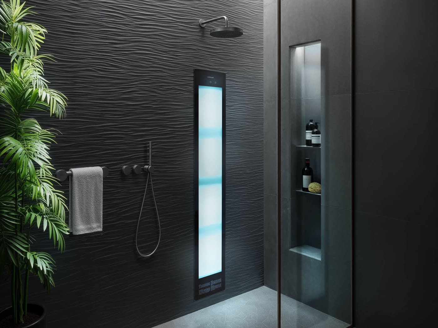 A dark shower lined in black wave-textured tile. A Sunshower panel glows cool blue and white beside matt black controls, a handshower and a grey towel on a rail, with a palm at the left and a lit niche behind the glass holding bottles.